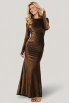 Full-length front view of model wearing the Aura bronze metallic mermaid gown with high round neckline and fitted sheer long sleeves, studio shot.