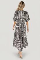 Model wearing Austin Kimono Midi Dress styled with sandals; view emphasizes tiered midi skirt and flowing movement in black print.