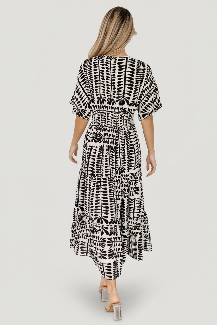 Model wearing Austin Kimono Midi Dress styled with sandals; view emphasizes tiered midi skirt and flowing movement in black print.