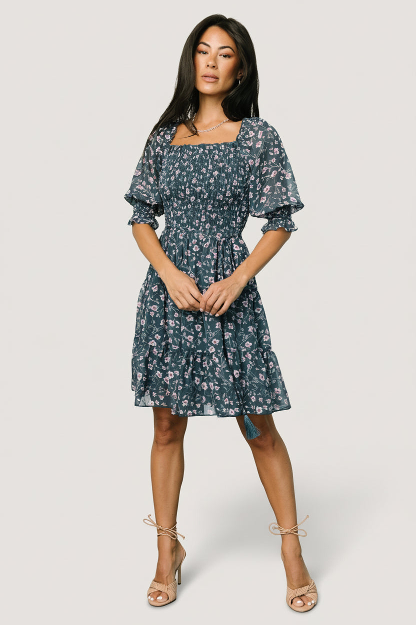 Back view of Azlyn dress in blue multi floral, featuring tiered skirt, gathered seams, and detached waist tie with tassel ends visible.