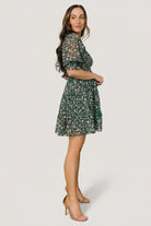 Detail view of semi-sheer sleeve and smocked ruffle cuff, plus the detachable waist tie with decorative tassels on the green floral dress.