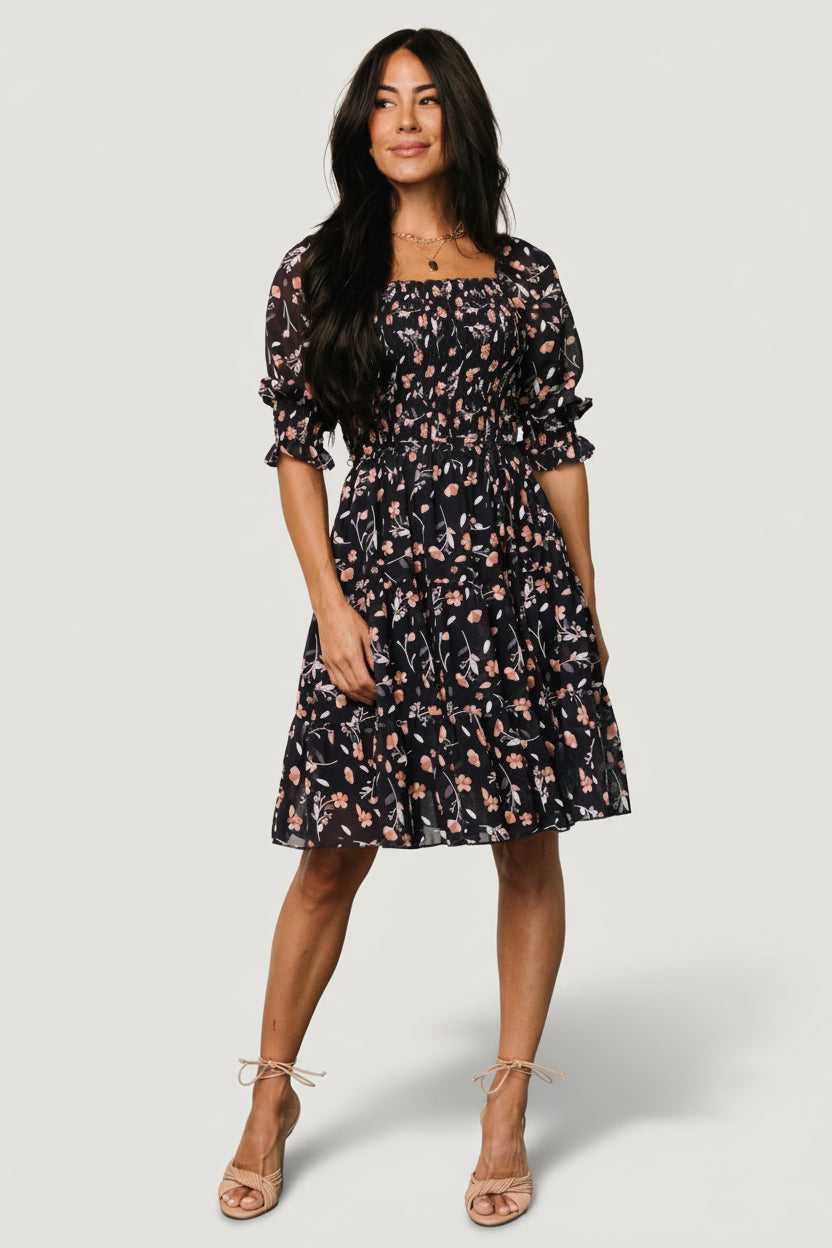 Front view of Azlyn smocked short dress in navy with pink floral print on a mannequin, showing ruffled square neckline and smocked bodice.