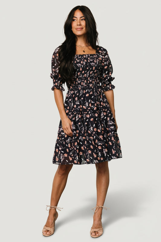 Front view of Azlyn smocked short dress in navy with pink floral print on a mannequin, showing ruffled square neckline and smocked bodice.