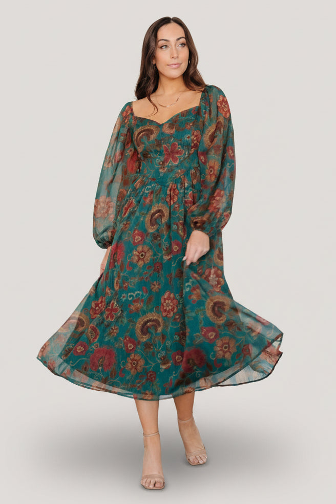 Front three-quarter view of Babette Basque Waist midi dress in deep teal with rust and green floral print worn on a model.