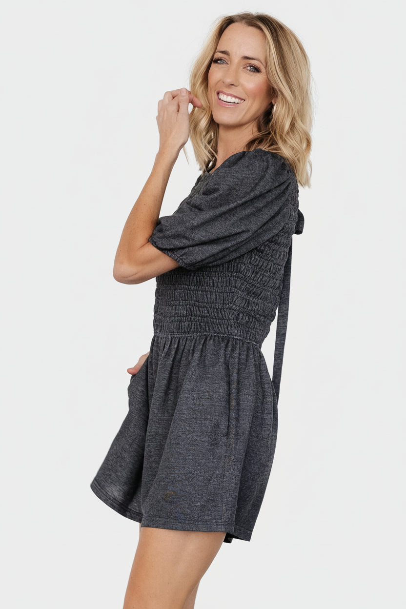 Styled outfit photo of Beaumont Romper in heather black with pockets visible and mid-length sleeves, shown with casual sandals for a relaxed look.