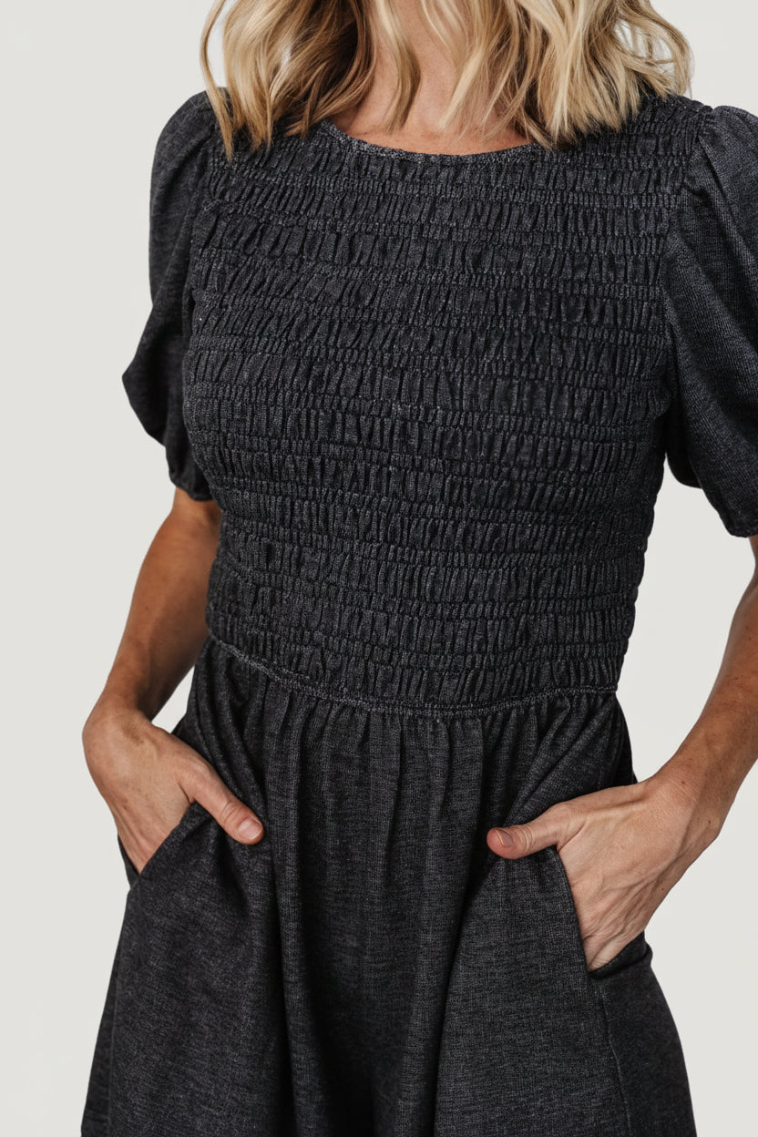 Close-up of Beaumont Romper fabric and smocked bodice showing stretch detail, elastic waist, and soft cotton-poly jersey knit texture in heather black.