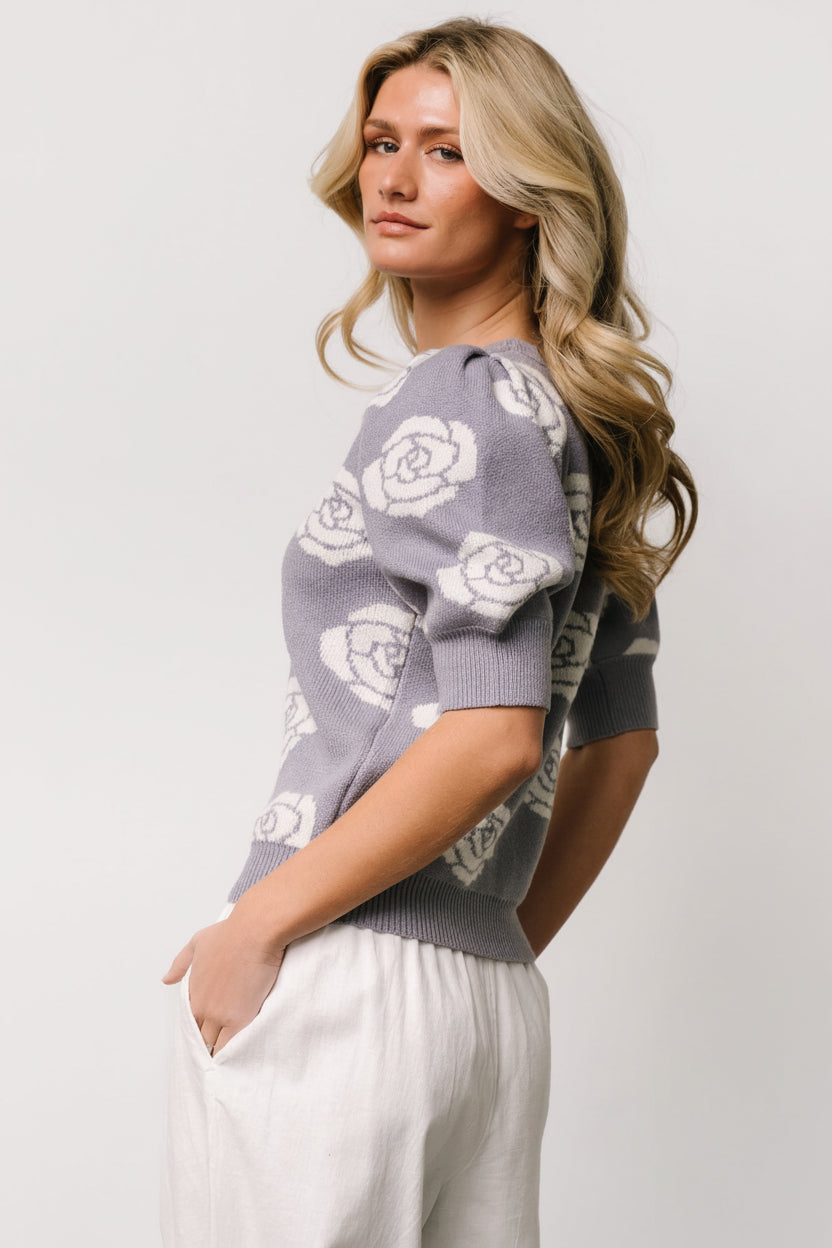 Close-up of dusty lavender knit fabric with cream floral pattern, ribbed neckline and textured bubbled sleeve for a feminine finish.