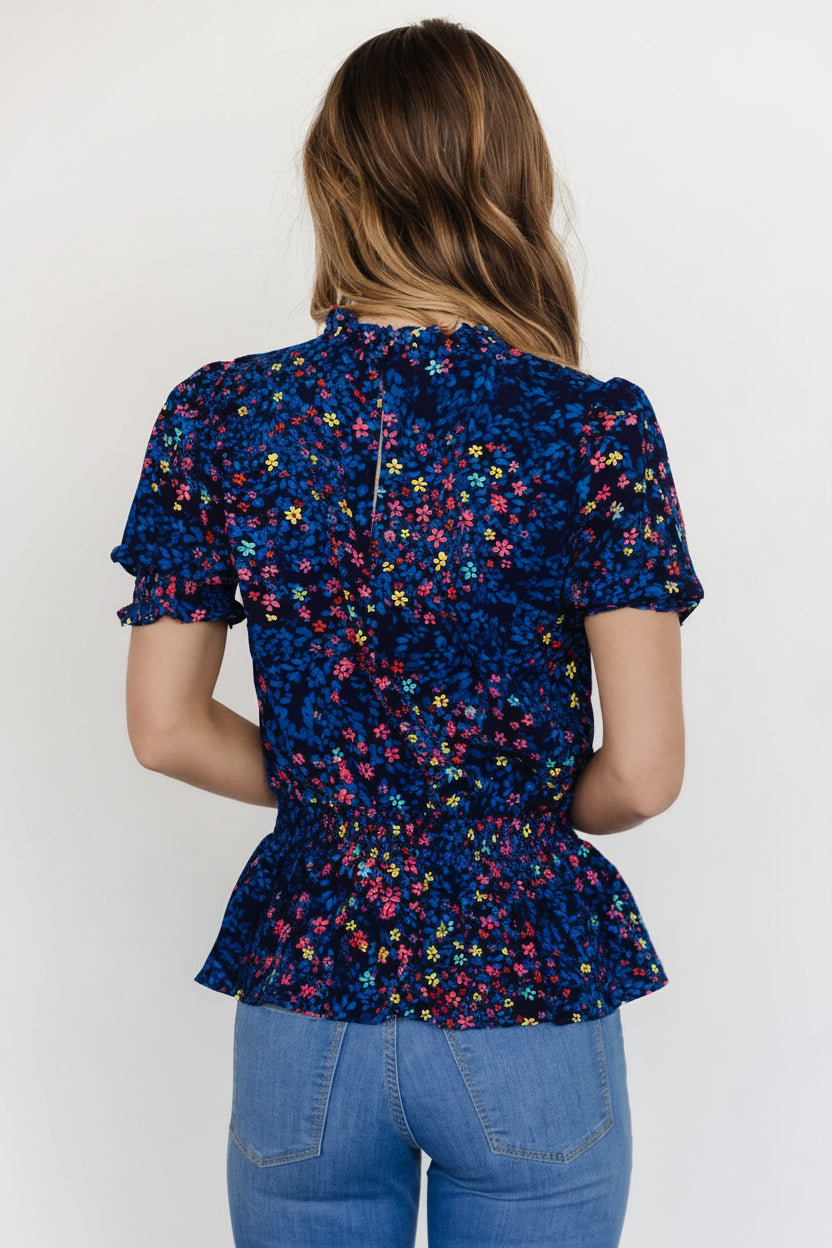 Detail of short ruffled sleeve with smocked cuff on blue multi floral peplum top, showing sleeve volume and stitching finish.