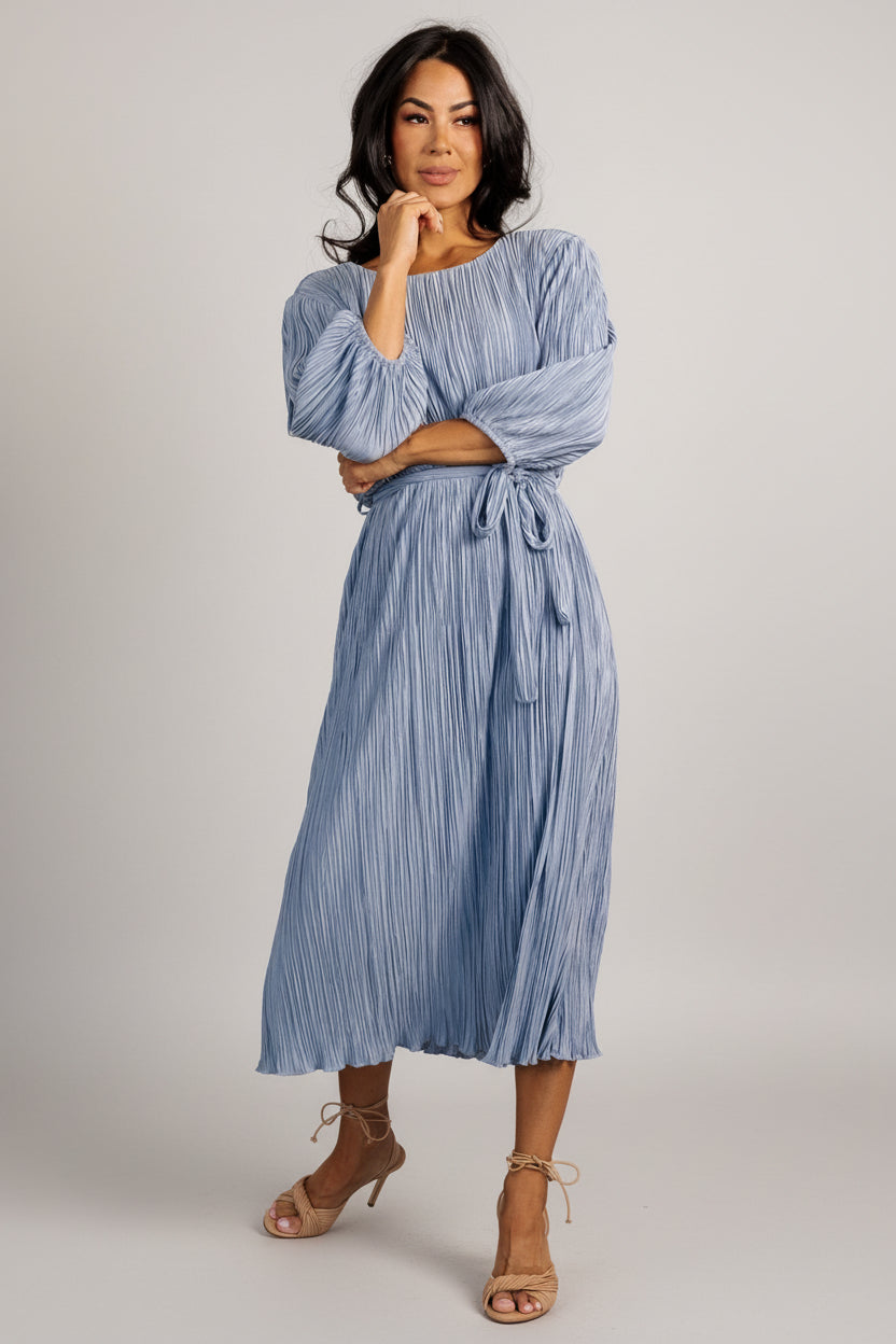 Back view of Bethany Pleated Midi Dress showing back-buttoned keyhole closure and smooth pleated skirt in dusty light blue fabric.