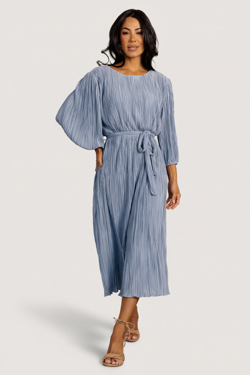 Front view of Bethany Pleated Midi Dress in dusty light blue on model, showing round jewel neckline, bloused bodice, and pleated skirt.