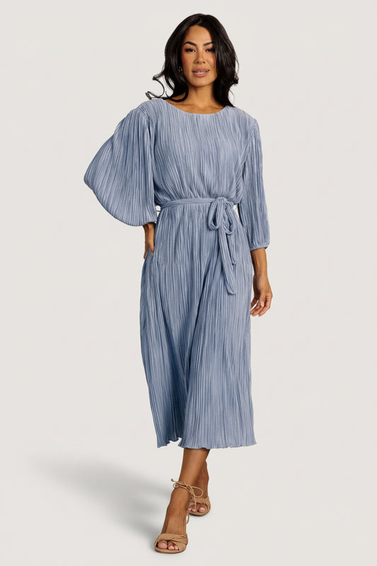 Front view of Bethany Pleated Midi Dress in dusty light blue on model, showing round jewel neckline, bloused bodice, and pleated skirt.