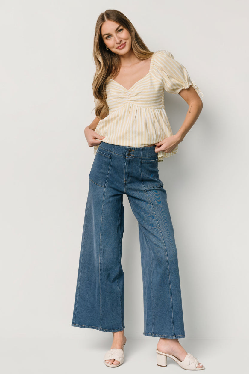 Side angle showing short oversized elastic sleeve with decorative tie detail and upturned waist peplum silhouette.
