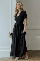 Model wearing the Birdie Maxi Dress in black, showing flutter sleeves and flowing skirt length for event-ready styling.