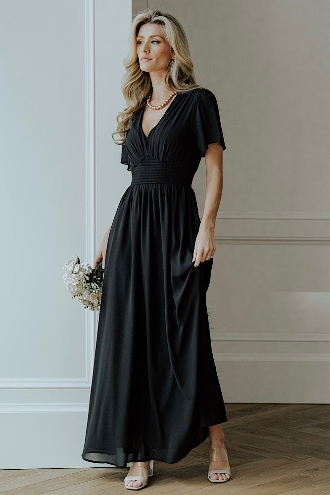 Model wearing the Birdie Maxi Dress in black, showing flutter sleeves and flowing skirt length for event-ready styling.