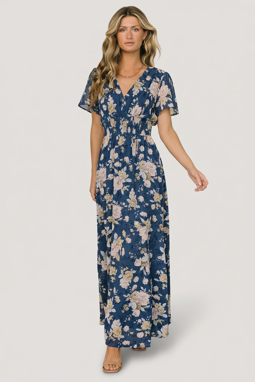Front model view of Birdie maxi dress in blue and blush floral print; chiffon-style polyester with V-neck, flutter sleeves, and smocked waist.