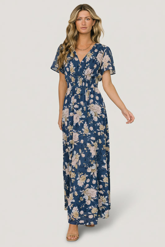 Front model view of Birdie maxi dress in blue and blush floral print; chiffon-style polyester with V-neck, flutter sleeves, and smocked waist.