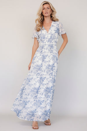 Front view of off-white chiffon maxi dress with light blue floral print, V-neckline, short flutter sleeves, and smocked waist.