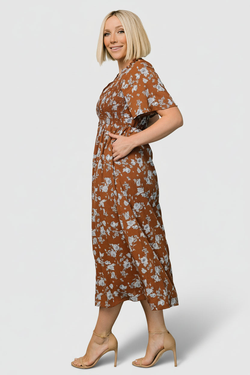 Close-up of the ruffled notched neckline, functioning button-up front, and smocked detailing at the front bodice in brown and blue floral print.