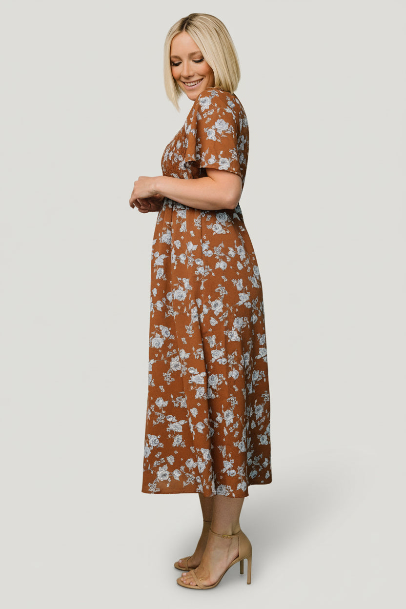 Full-length shot of the brown and blue floral midi on model showing fit through the bodice, defined waist, and graceful midi hemline.