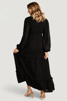 Side view of the black Bowman dress emphasizing the subtle leg slit, tiered skirt movement, and lightweight polyester chiffon.