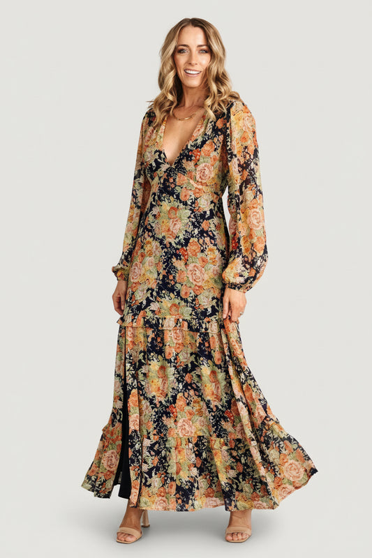 Front view of navy floral chiffon maxi dress with deep V-neck, long sleeves, elastic back waist and ruffle-tiered skirt with side slit.