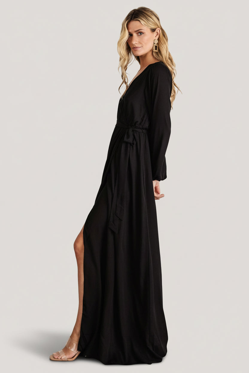 Full-length shot of the black faux-wrap maxi dress on a model, showing the long sleeve fit and flowing skirt.