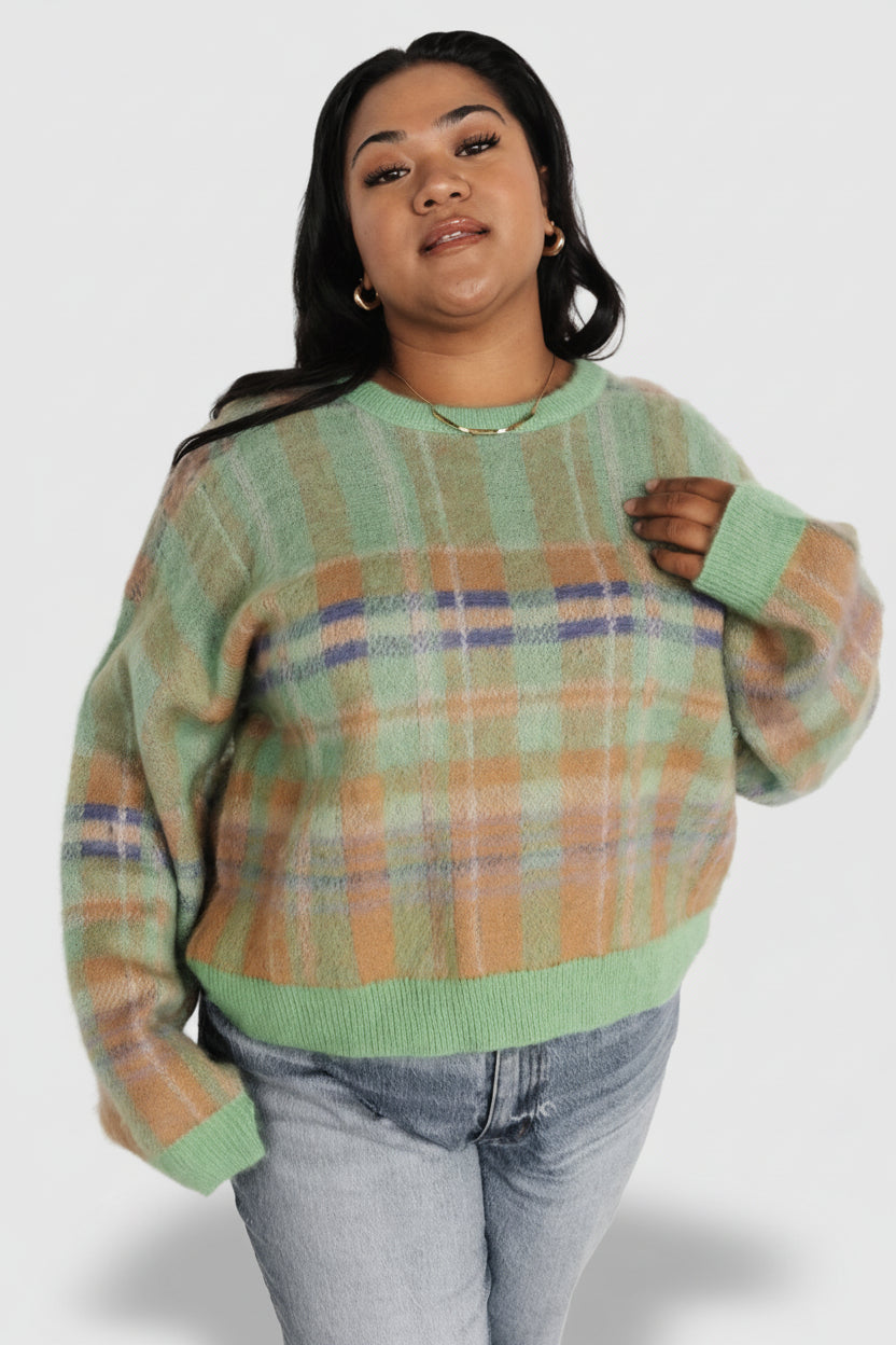 Three-quarter view of green multi plaid sweater showing drop shoulder sleeve, relaxed silhouette, and colorful plaid panels in soft knit.