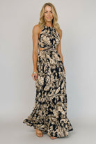 Model wearing navy tropical-print halter maxi dress; tied neck, elastic back waist, and tiered flowing skirt for breezy movement.