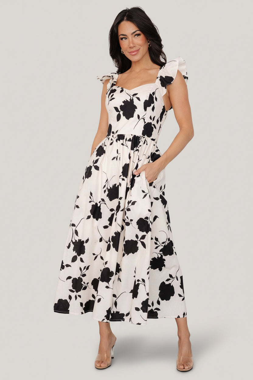 Front view of ivory midi dress with black floral print on model, showing sweetheart neckline, ruffled sleeves, and midi skirt with pockets.