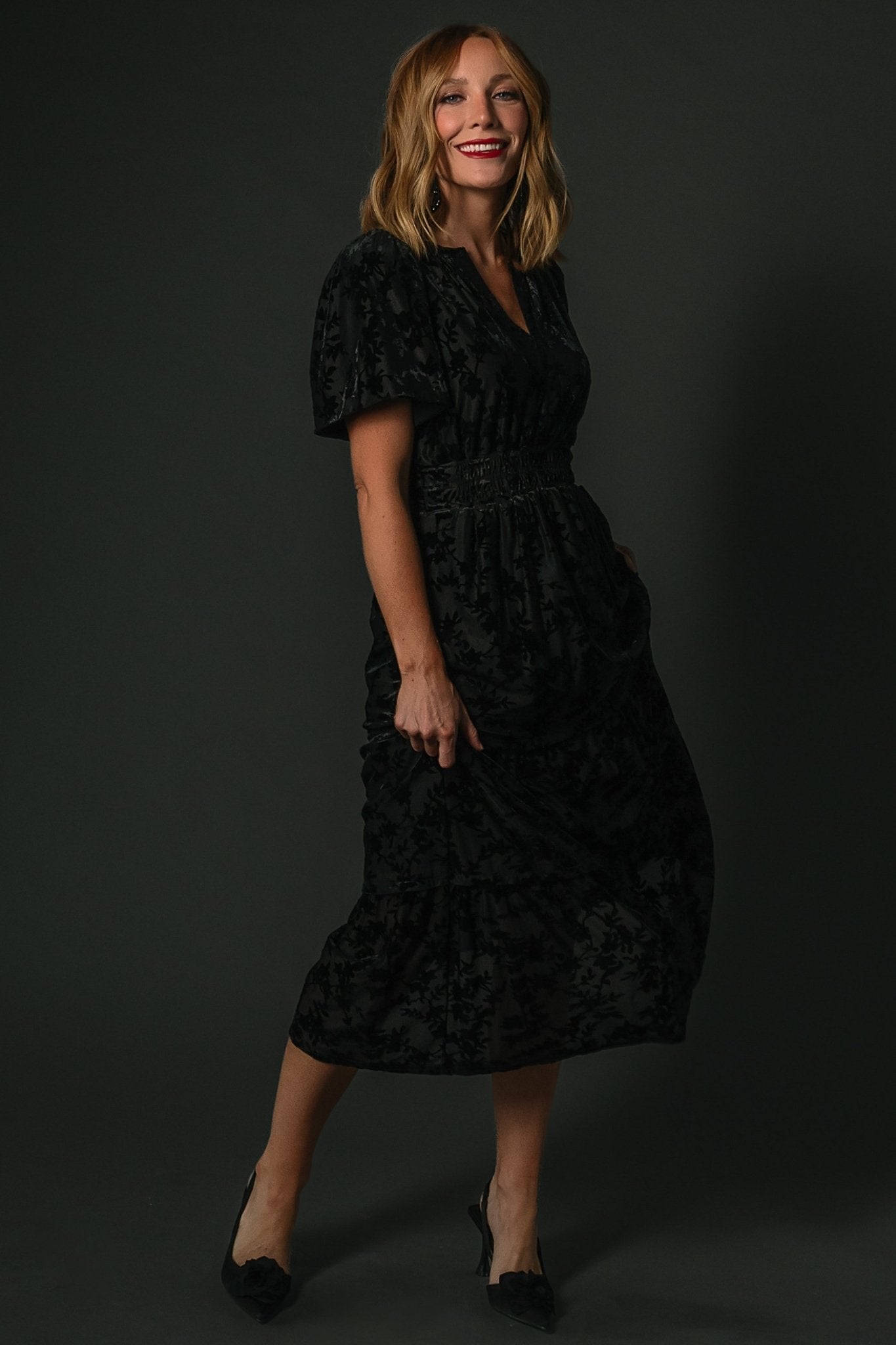 Side view of the Bronwyn midi dress in black highlighting a hidden side pocket and the two-tier skirt drape.