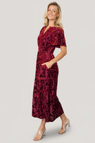 Model styling Bronwyn rust floral dress with hands in hidden side pockets, demonstrating pocket placement and relaxed midi length.