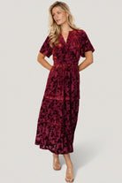 Full-length view of the Bronwyn burnout velvet midi dress in rust floral print on model, showing overall silhouette and flutter sleeves.
