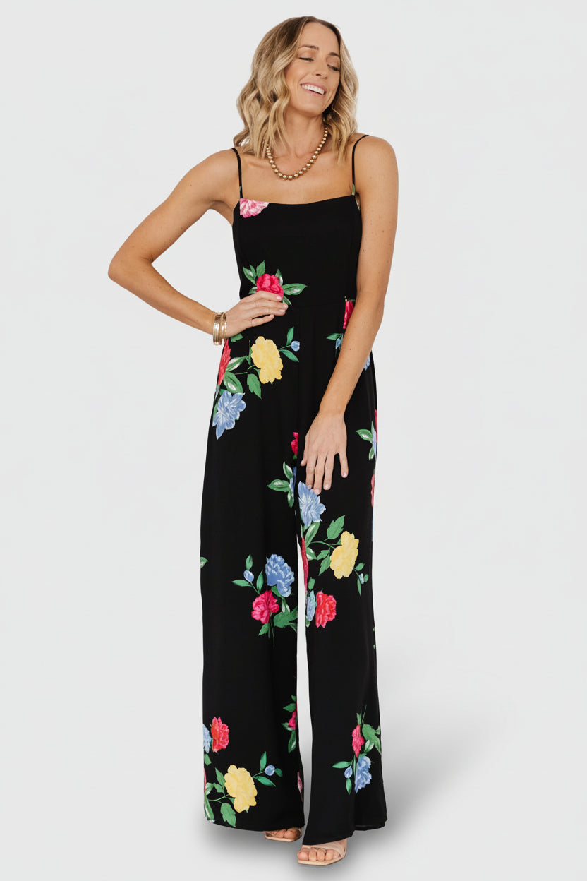 Front view of black floral wide-leg jumpsuit with square neckline, adjustable spaghetti straps, flowing chiffon fabric and full lining for coverage.