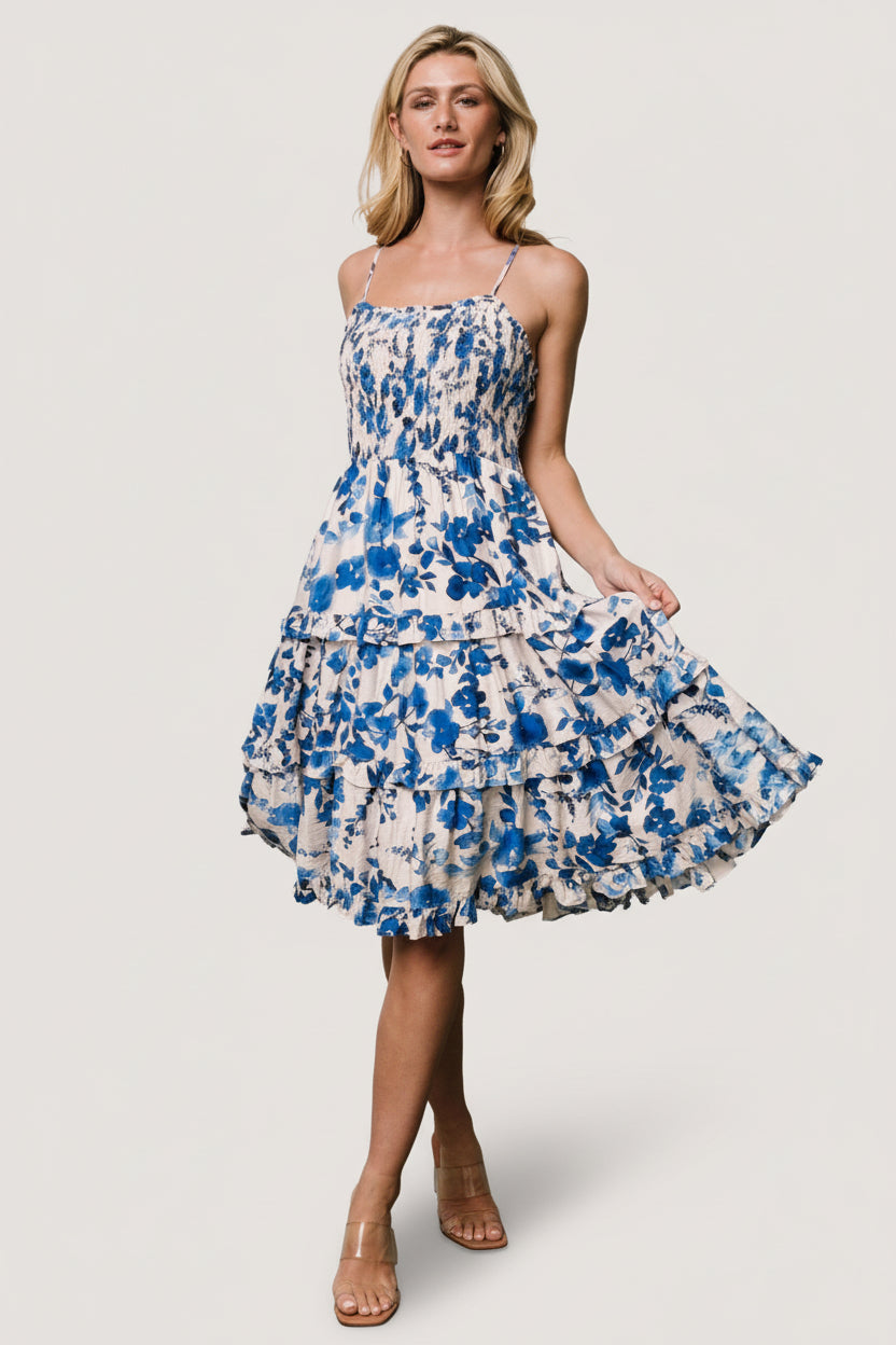 Front view of Calina tiered midi dress in ivory with blue floral print, smocked bodice, ruffled square neckline, adjustable straps, and side pockets.