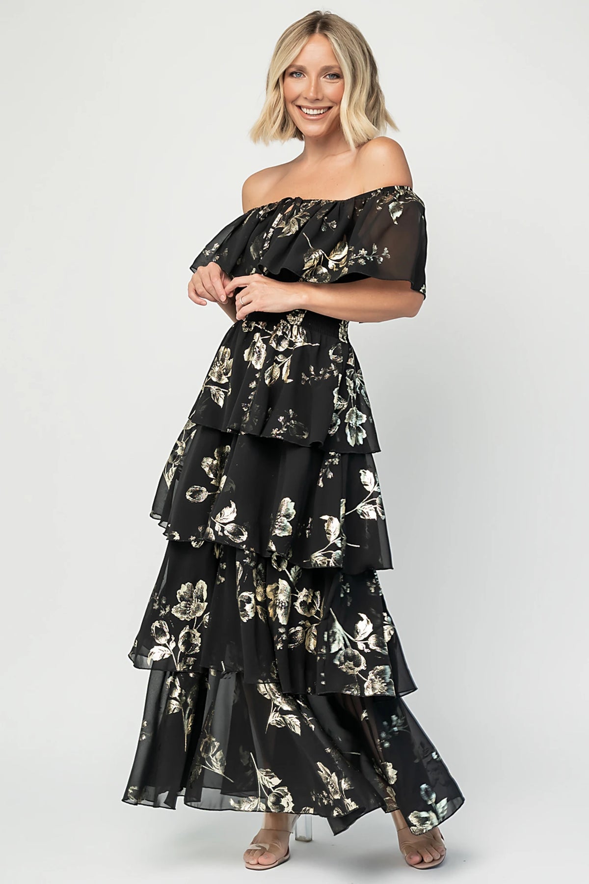 Carina Off Shoulder Maxi Dress in Black + Gold with floral print, ruffle neckline, smocked waist, and tiered chiffon skirt.
