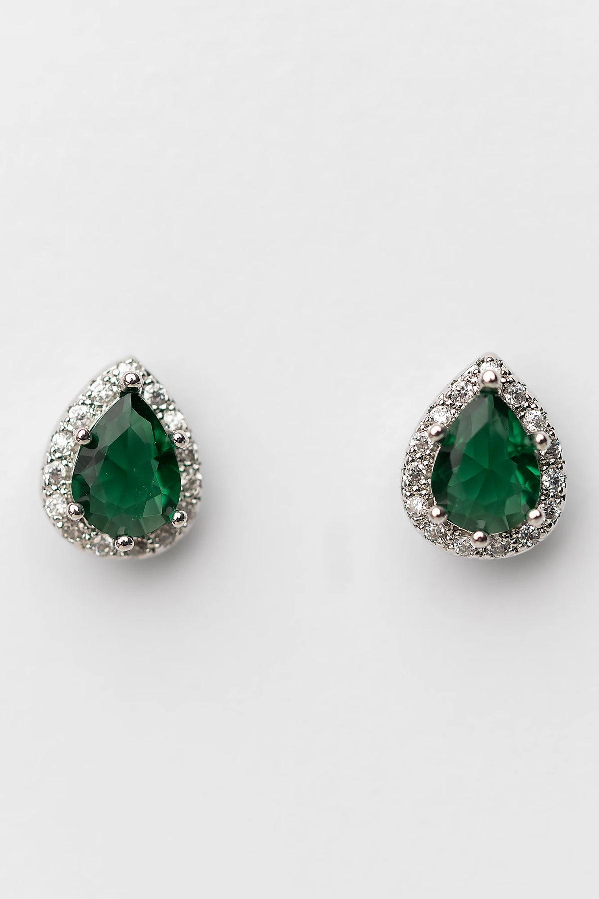 Dacia Pear Cut Stud Earrings in Emerald with pear-cut green stones, clear stone halos, and silver-tone settings.