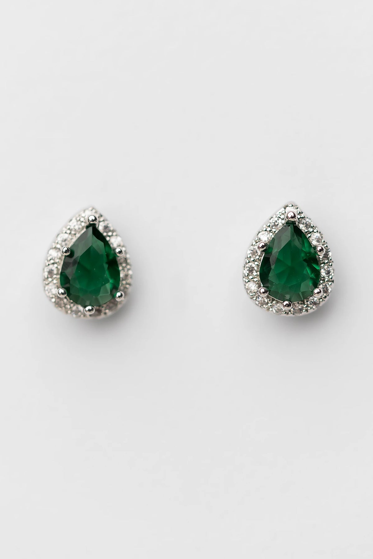 Dacia Pear Cut Stud Earrings in Emerald with pear-cut green stones, clear stone halos, and silver-tone settings.
