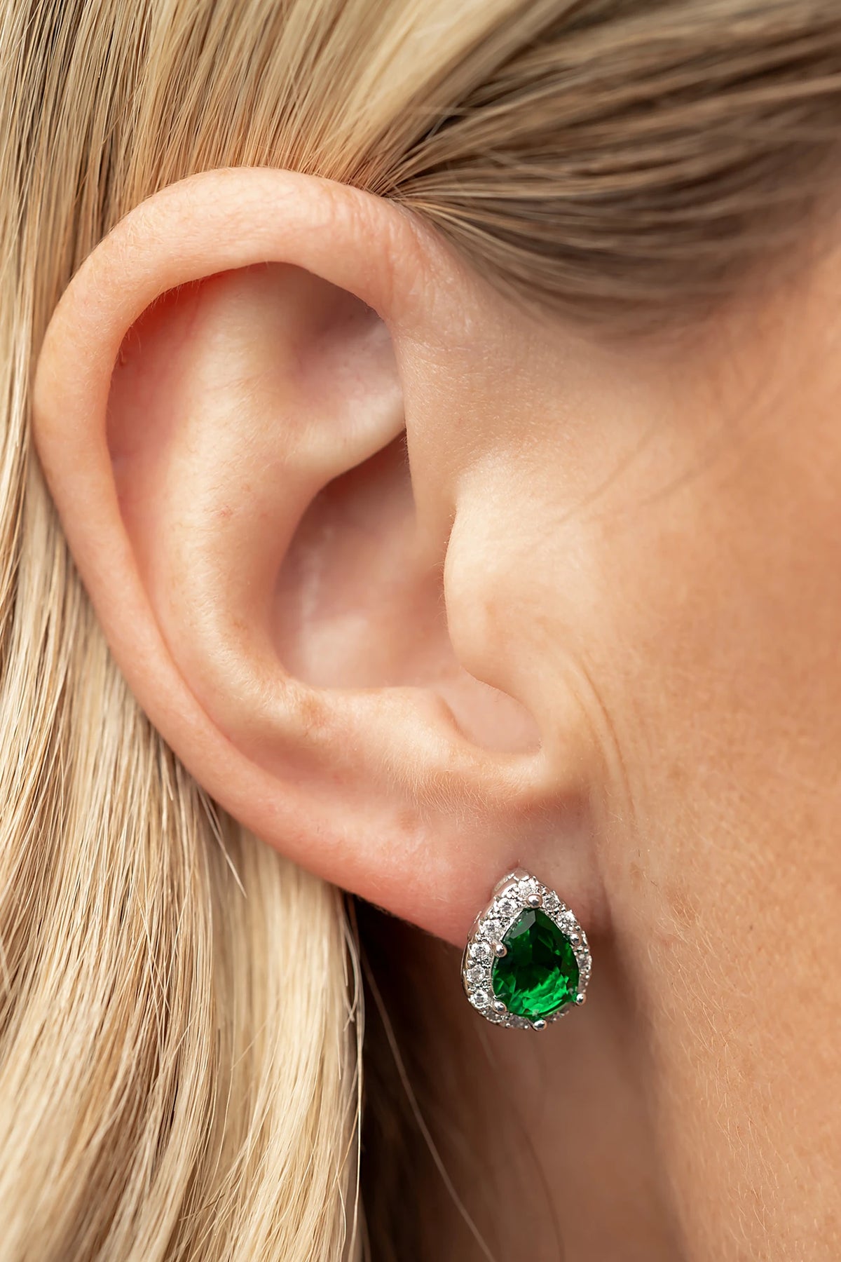 Dacia Pear Cut Stud Earrings in Emerald with pear-cut green stones, clear stone halos, and silver-tone settings.