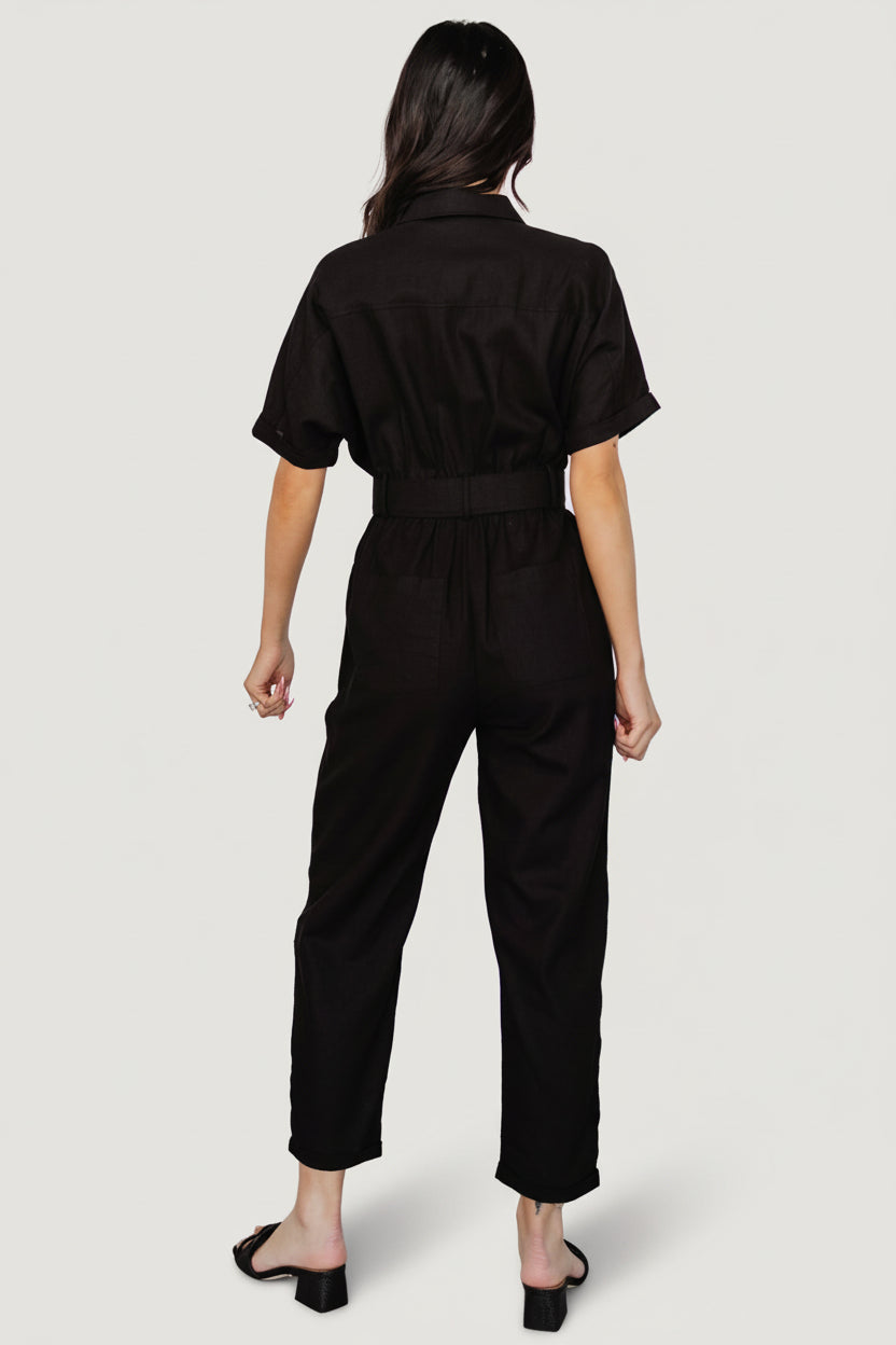 Back and side styling of the black linen jumpsuit, illustrating the relaxed utility fit and belt-loop waist with removable sash styling option.