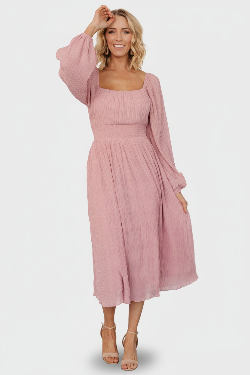Front view of model wearing Dalton pleated midi dress in blush showing Florentine neckline and A-line skirt, fully lined.