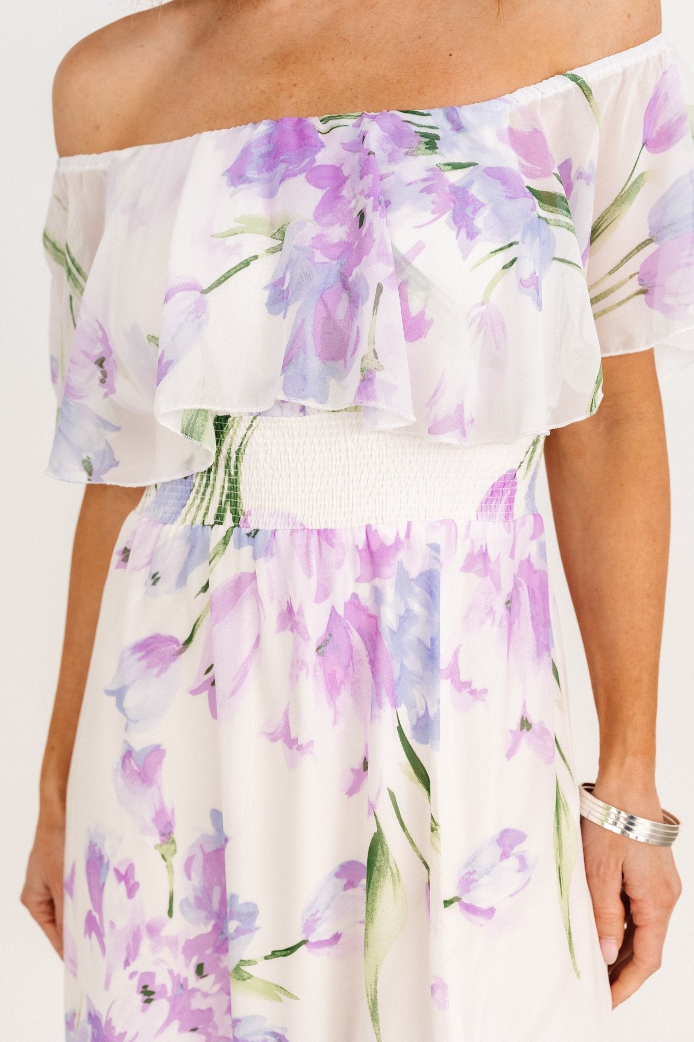 Side view of the Daphne maxi showing drape and left-side slit, ivory base with lavender and purple floral pattern and flowing chiffon layers.