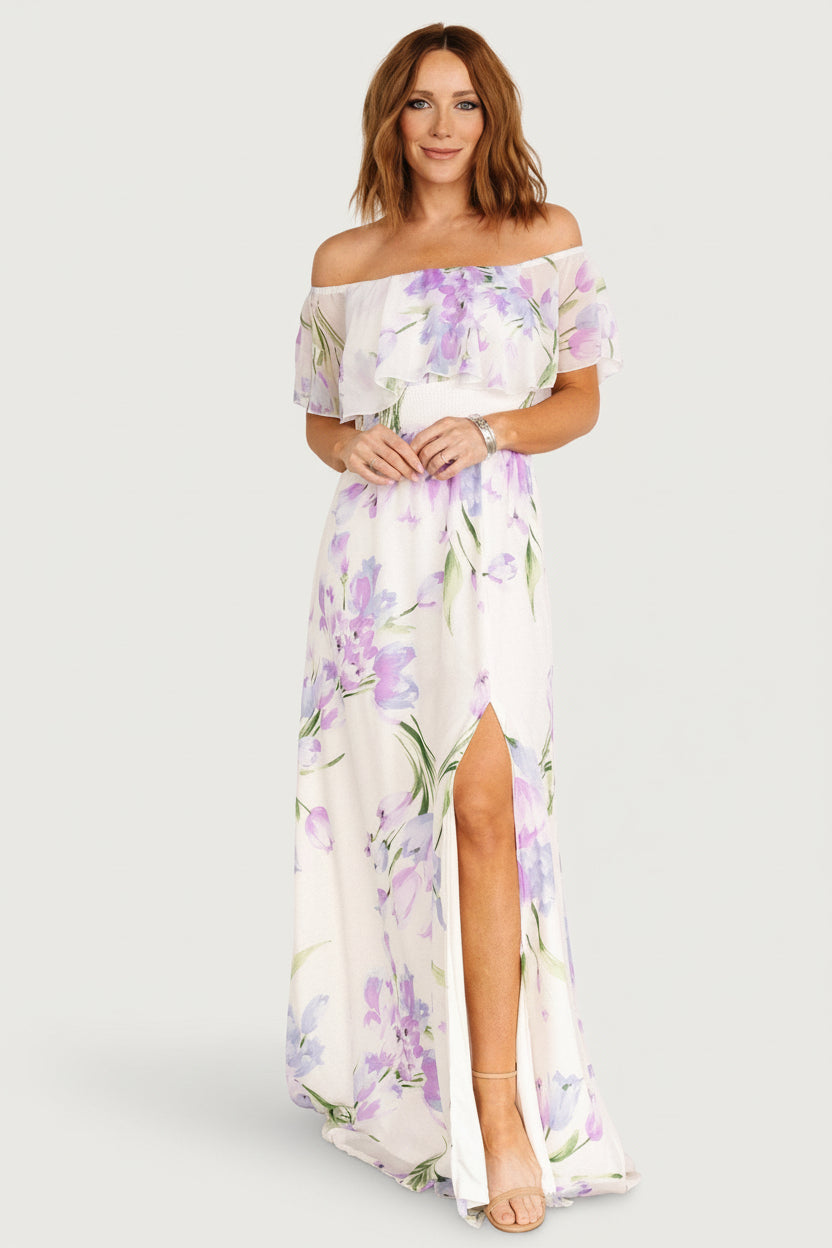 Front view of Daphne off-shoulder ivory maxi dress with lavender and purple floral print, ruffled elastic neckline and smocked waist.