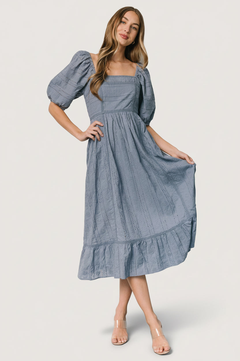 Model in dusty blue Delaney Eyelet Midi Dress — full-length view showing Florentine neckline, smocked back, and tiered skirt.