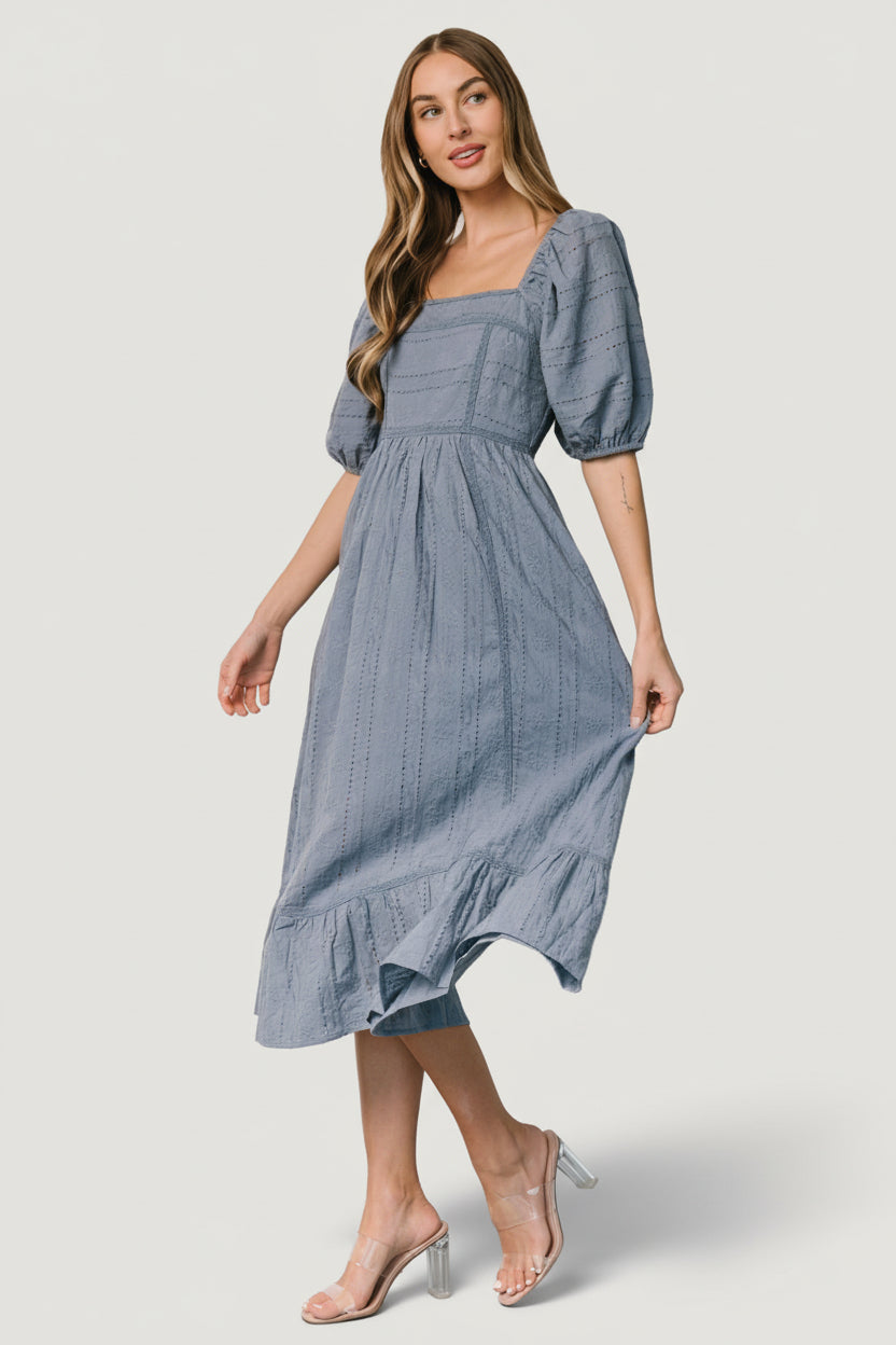 Model styling the Delaney Eyelet Midi Dress in dusty blue with sandals, showing movement and natural drape of cotton.