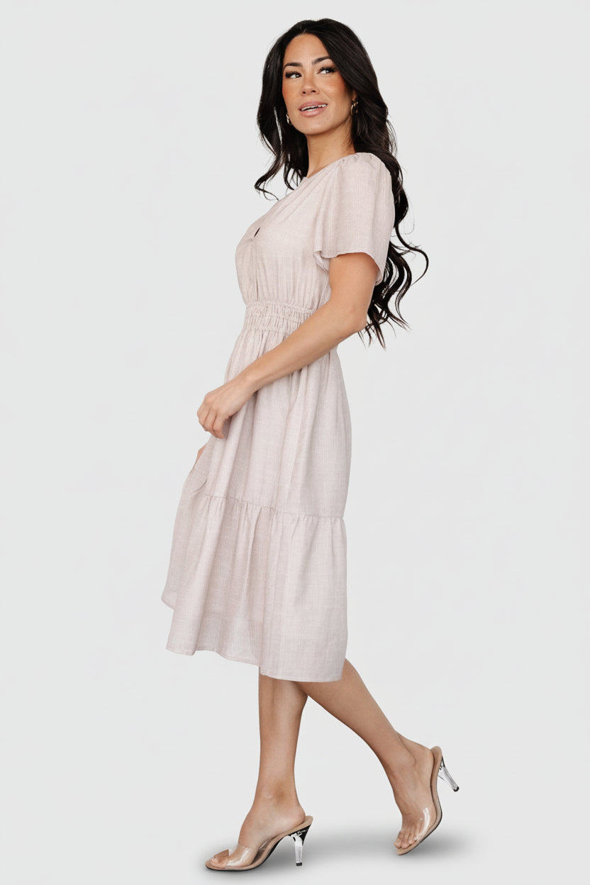 Model wearing Dita short dress in natural check, styled with casual shoes to show length, fit, and smocked waist shaping on a real body.