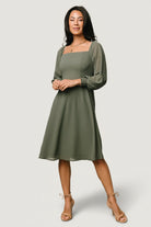 Front view of a short dark sage chiffon dress with smocked back bodice and lined skirt, on a studio mannequin