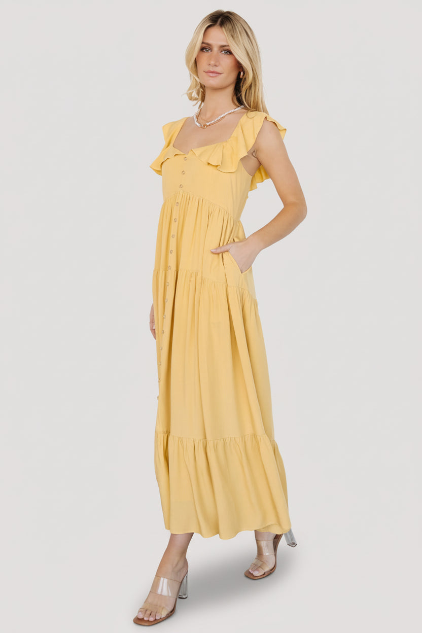 Front view of golden yellow ruffle top midi dress on model showing wide V-neck, layered ruffle and tiered skirt in natural light.