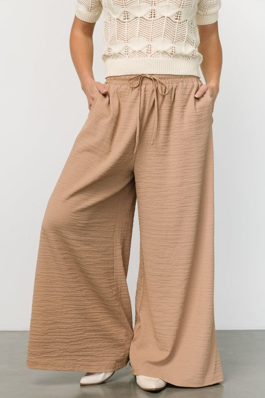 Beige puckered gauze wide-leg pants with elastic drawstring waist and hip slash pockets, worn standing.