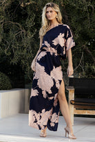 Front view of Halston one-shoulder maxi dress in navy and blush, showing dramatic statement sleeve, left-side cutout, right-side zipper, and flowing skirt.