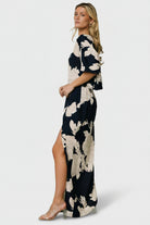 Model walking in navy-and-cream one-shoulder maxi dress, showcasing movement of the flowing skirt and left-side slit.